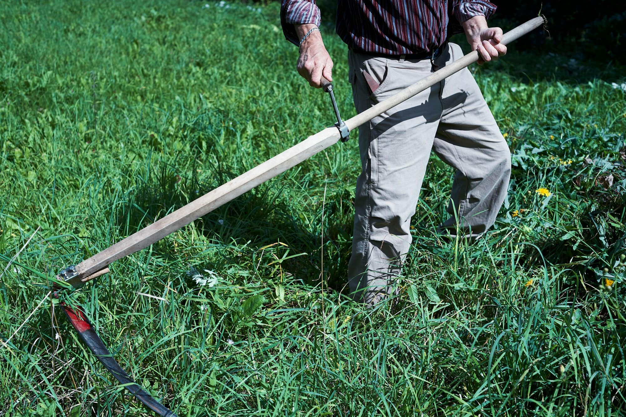 Person cutting down knee-high grass in an overgrown yard with a long-handled tool